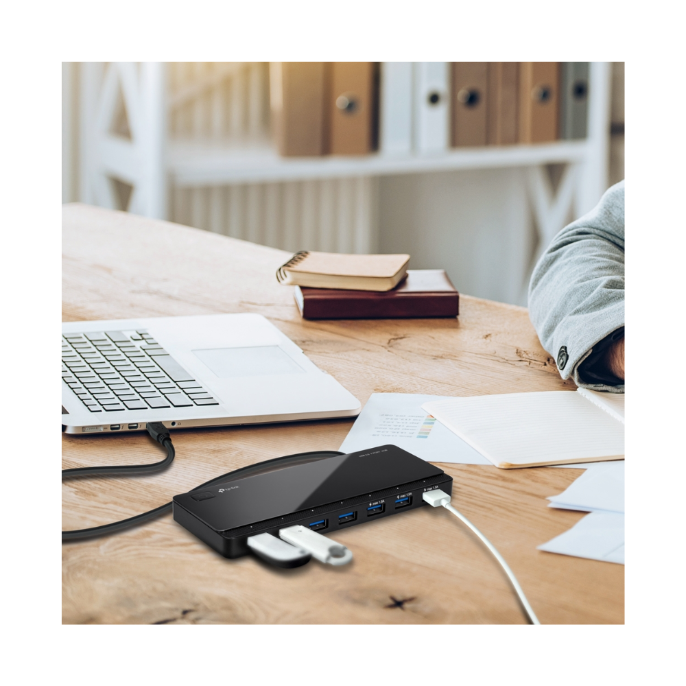 USB hub on a desk with a laptop and books in the background